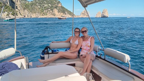 Two women sitting on a boat with a scenic view of cliffs and ocean in the background.