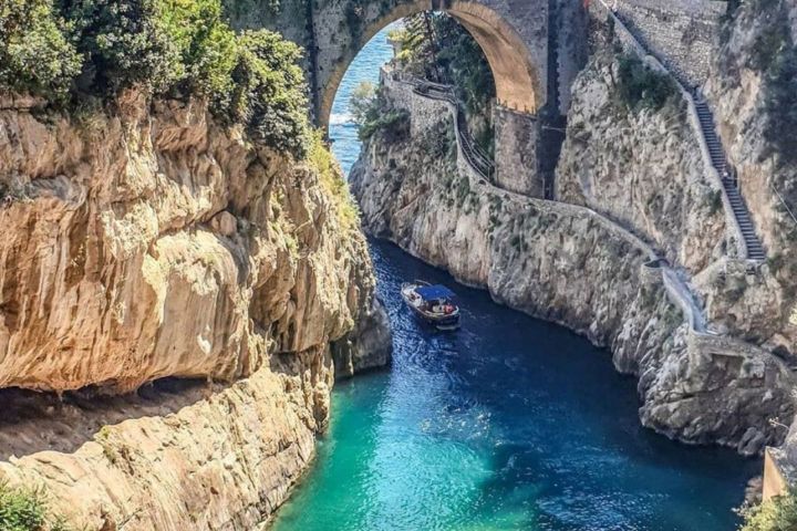 Scenic coastal arch bridge over turquoise water with beach and sunbathers below.