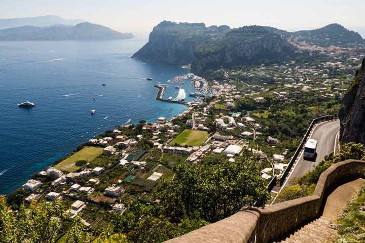 Scenic coastal view with cliffs, buildings, and a road winding near a blue sea.