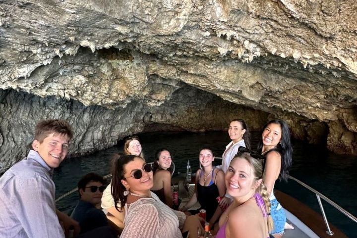 Group of people on a boat inside a rocky cave, smiling and relaxing.