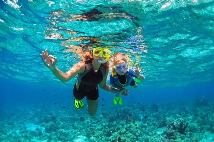 Two people snorkeling underwater, wearing masks and showing hand gestures near coral.