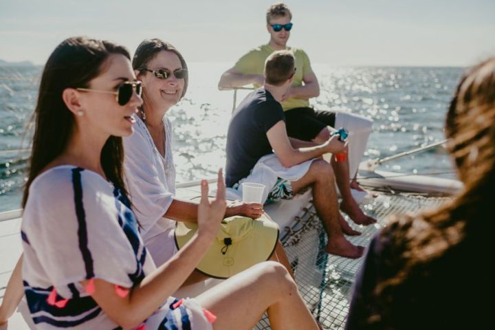 People relaxing and talking on a sailboat in sunny weather with ocean in background.