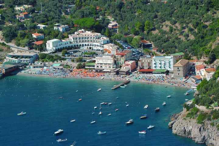 Aerial view of a coastal town with beaches, boats, and hillside buildings.