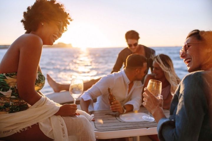 Group of friends laughing and drinking on a boat at sunset.