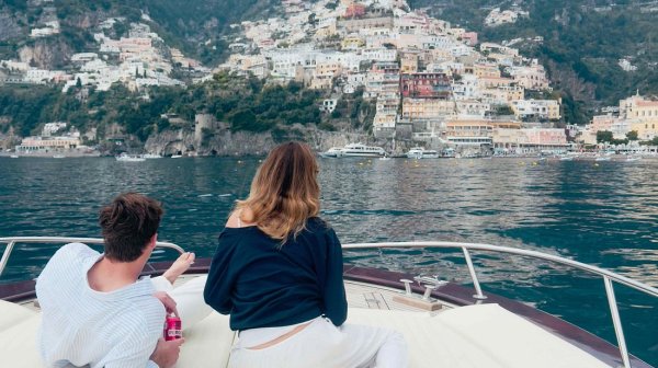 Two people on a boat gazing at colorful hillside town by the sea.