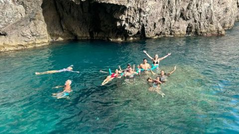 Group of people swimming in clear blue water near rocky cliff.