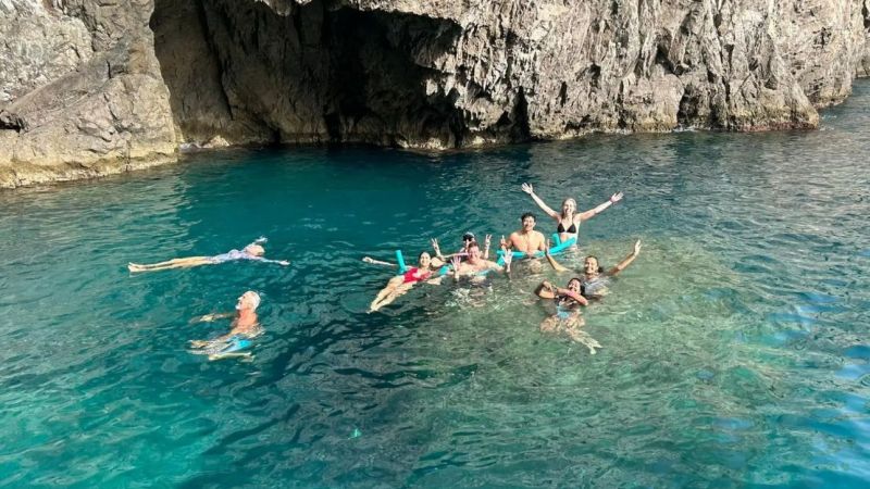 Group of people swimming in clear blue water near rocky cliff.
