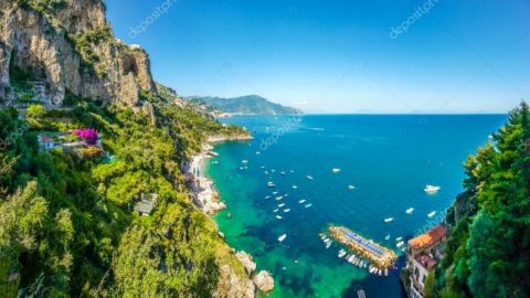 Cliffside view of a coastal landscape with clear blue sea and boats.