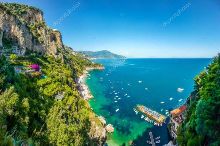 Cliffside view of a coastal landscape with clear blue sea and boats.