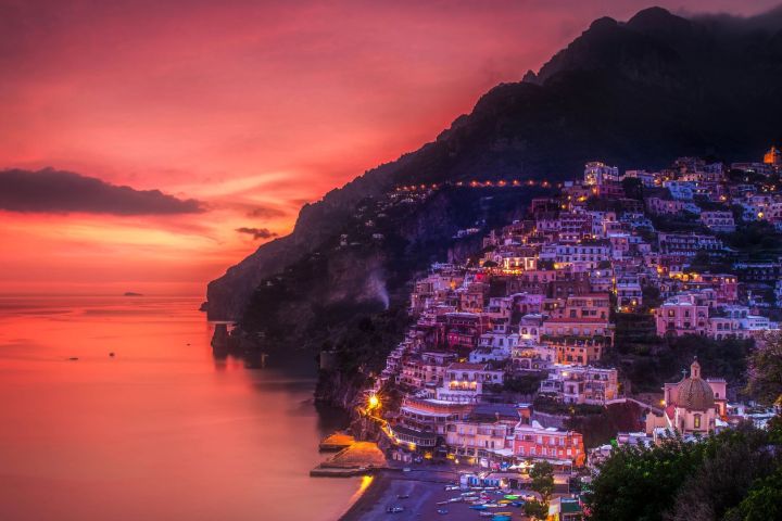 Colorful seaside town on cliffside at sunset with vibrant sky.