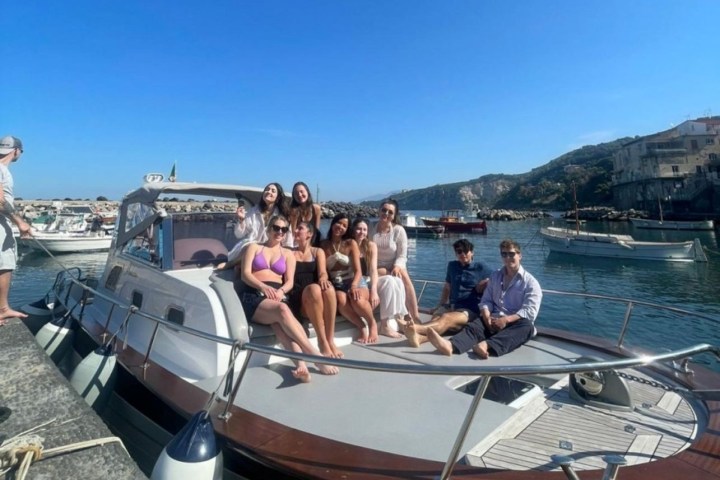 Group of people sitting on a boat docked at a waterfront with a clear blue sky.