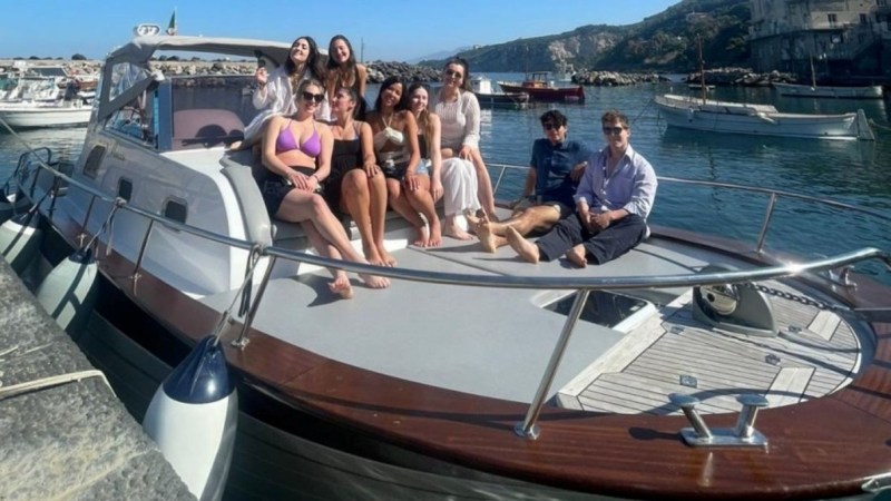 Group of people sitting on a boat docked at a harbor on a sunny day.
